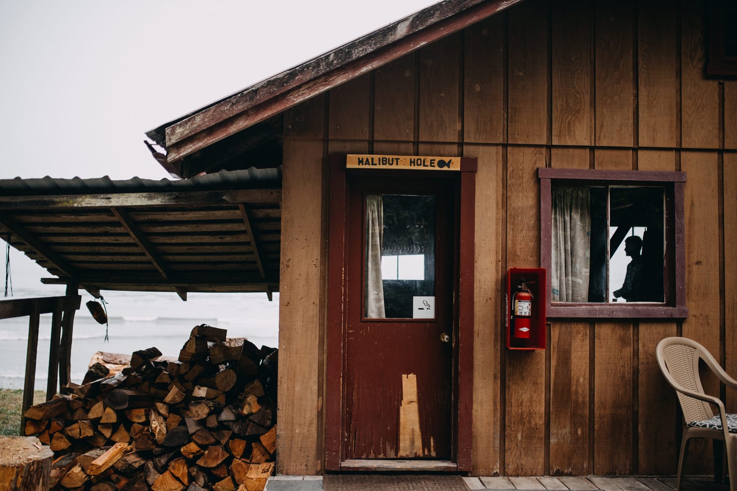 cabin in the olympic peninsula where you can see the groom's shadow silhouette in the window as he's getting ready with a a sign that says "halibut hole" above the door by marcela pulido portland wedding photographer