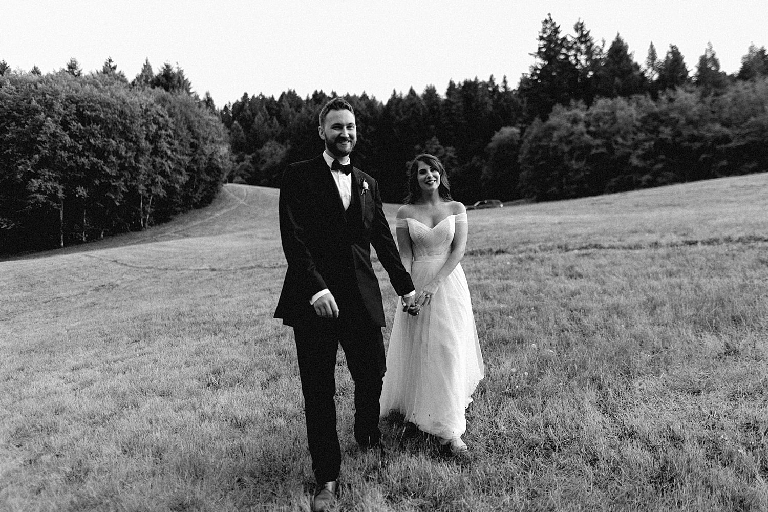 black and white image of a bride and groom newlyweds walking in an open field captured by portland wedding photography pricing by marcela pulido