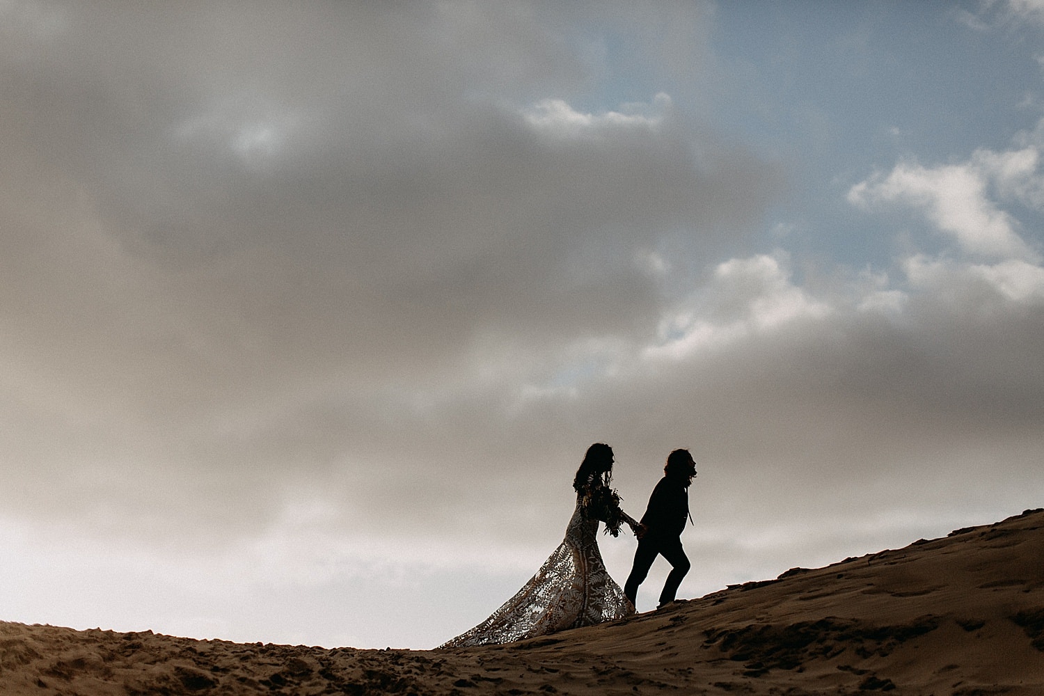 silhouette shot of newlywed couple on a sand dune against the stormy sky on oregon coast cape kiwanda elopement by marcela pulido portland oregon wedding photography