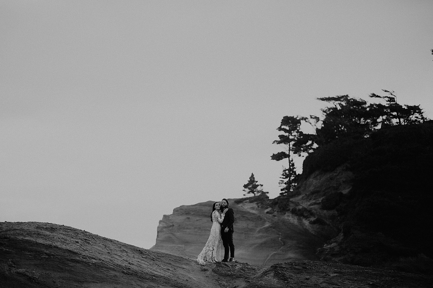 black and white photo of bride and groom on the oregon cliffside cape kiwanda elopement by marcela pulido portland oregon wedding photography