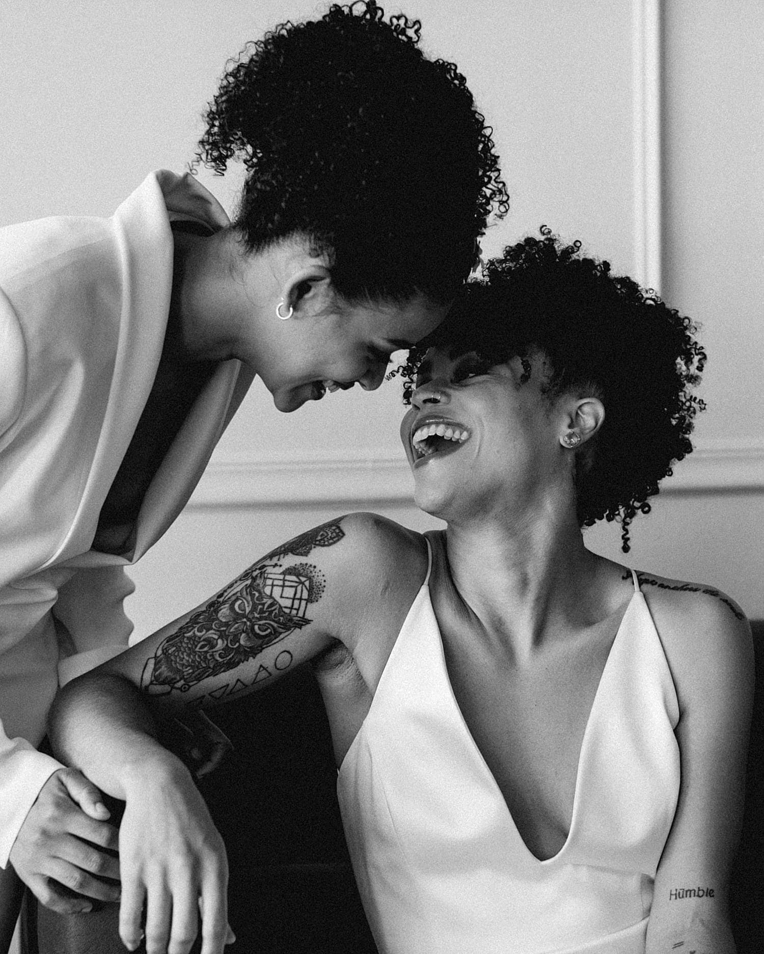 black and white smiling portrait of beautiful same sex lesbian lgbtq+ friendly wedding couple newlywed wearing all white gown and all white feminine suit
