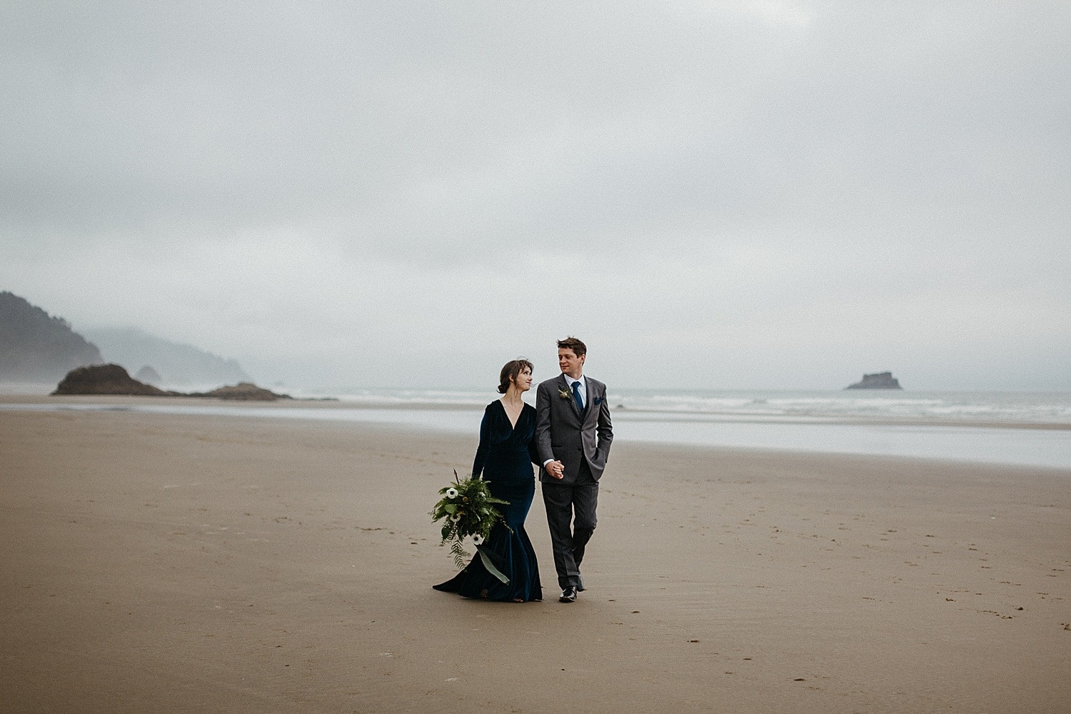 newlywed couple on the oregon coast walking hand in hand captured by marcela pulido photography portland oregon wedding elopement photographer