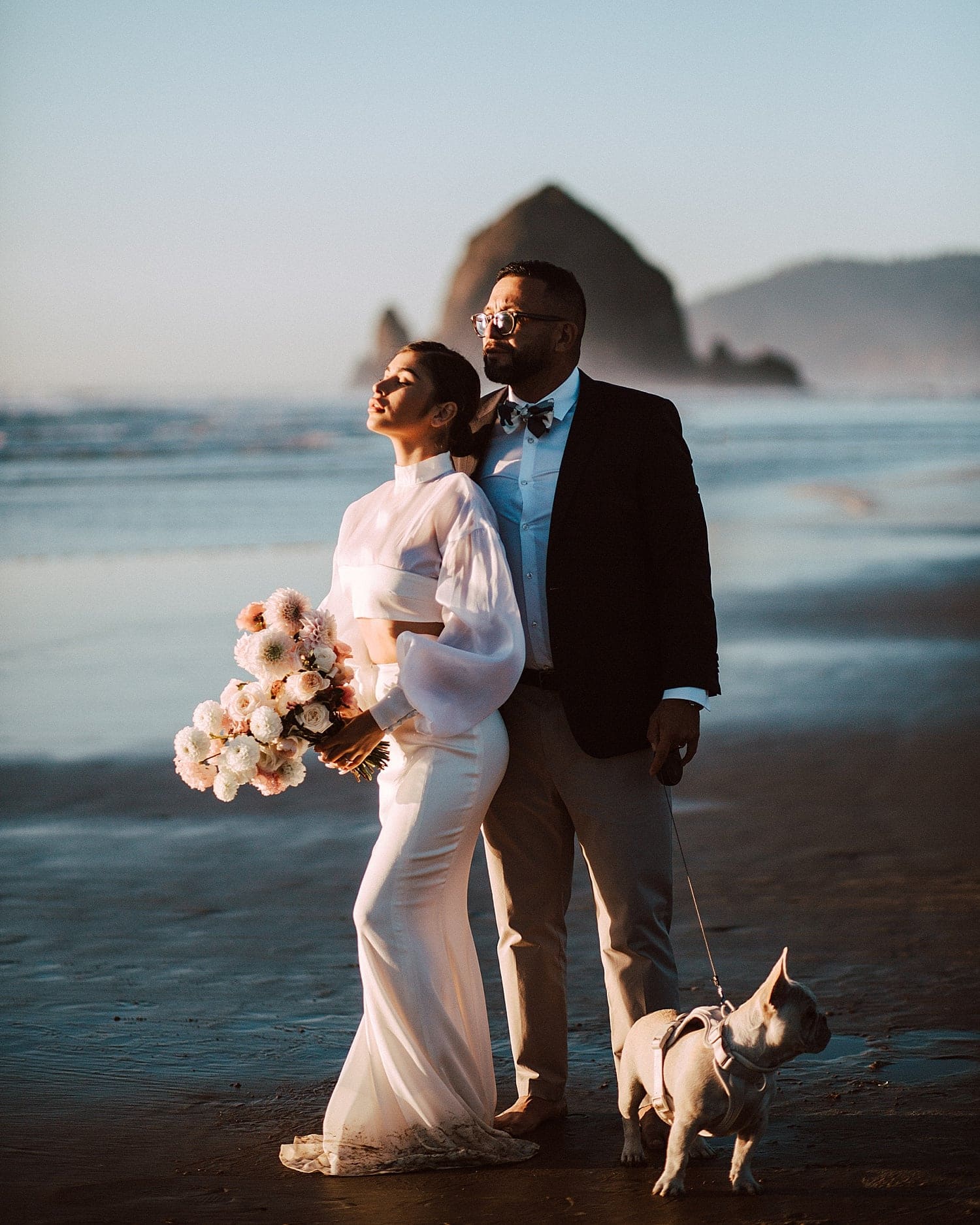 ethereal cinematic portrait of newlywed couple with their french bulldog puppy at cannon beach captured by marcela pulido portland oregon wedding photographer