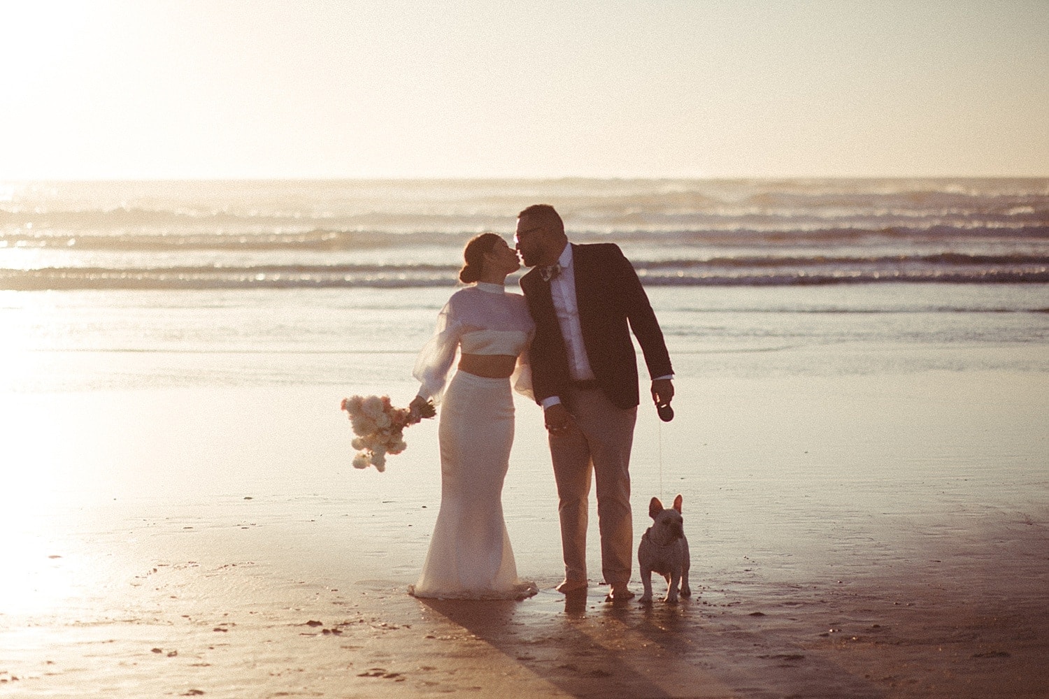 dreamy cinematic golden hour portrait of luxury high end couple with their french bulldog at cannon beach on the oregon coast captured by marcela pulido portland oregon wedding photographer