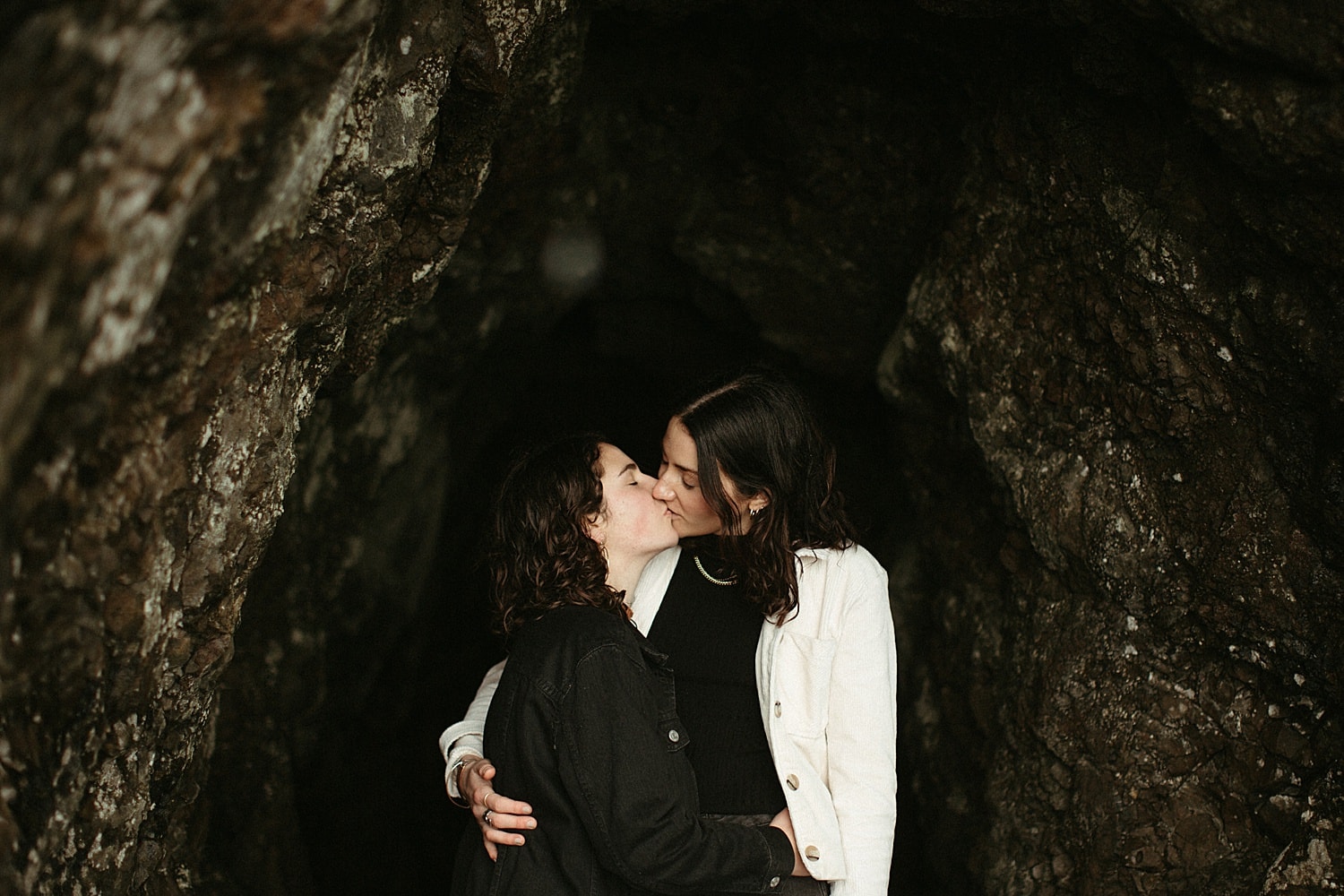 romantic and cinematic shot of a same sex couple framed by a cave on the Oregon Coast by Marcela Pulido Portland Wedding Photographer