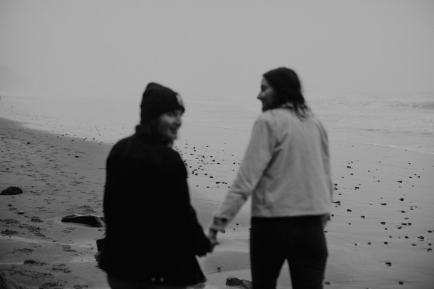black and white cinematic shot of a lesbian same sex lgbtq+ couple holding hands and walking on the beach by Marcela Pulido Portland Wedding Photographer